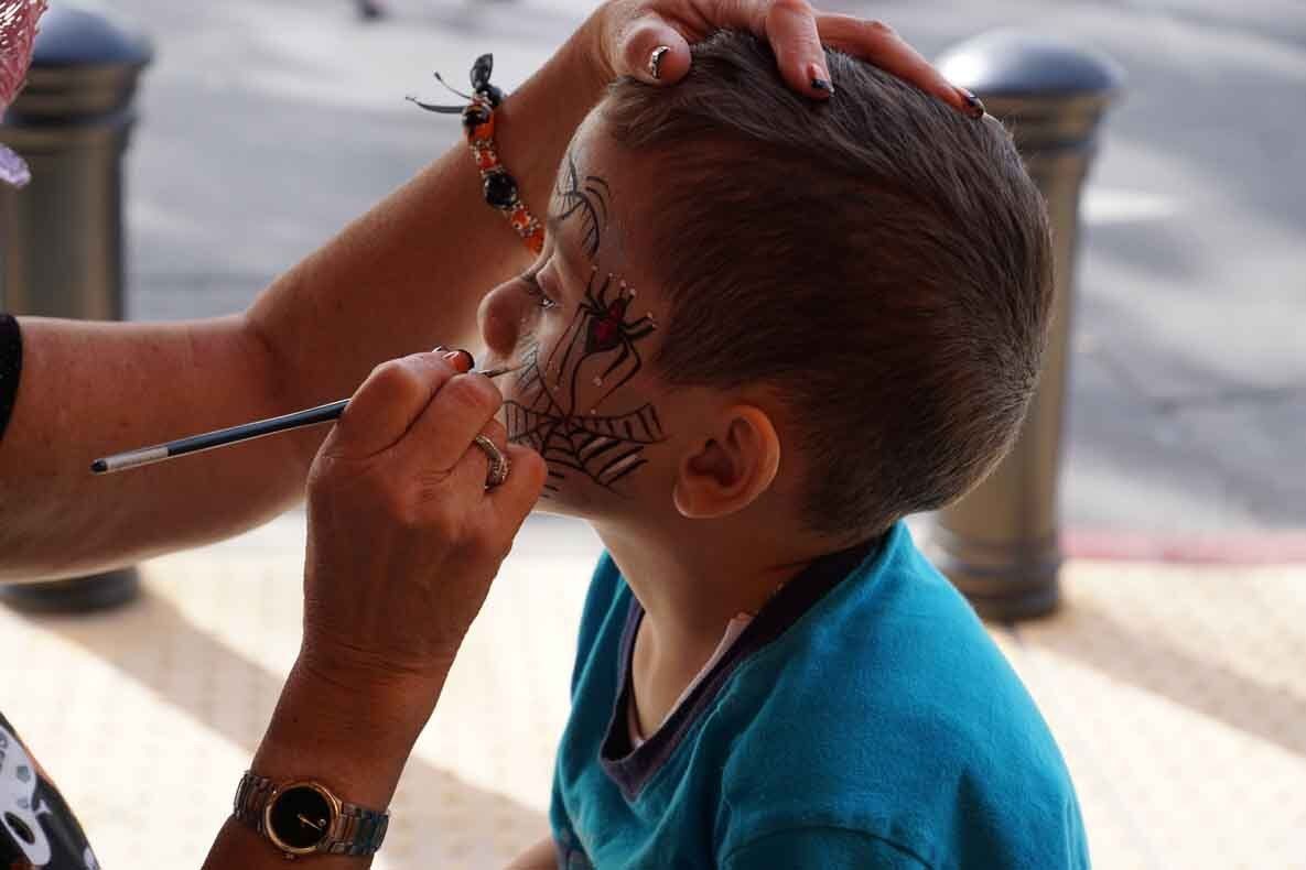 A young boy is getting his face painted with a spider on it