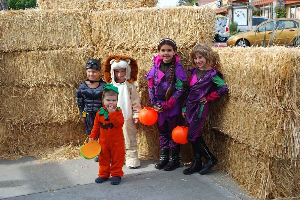 A group of children in halloween costumes are standing next to hay bales.