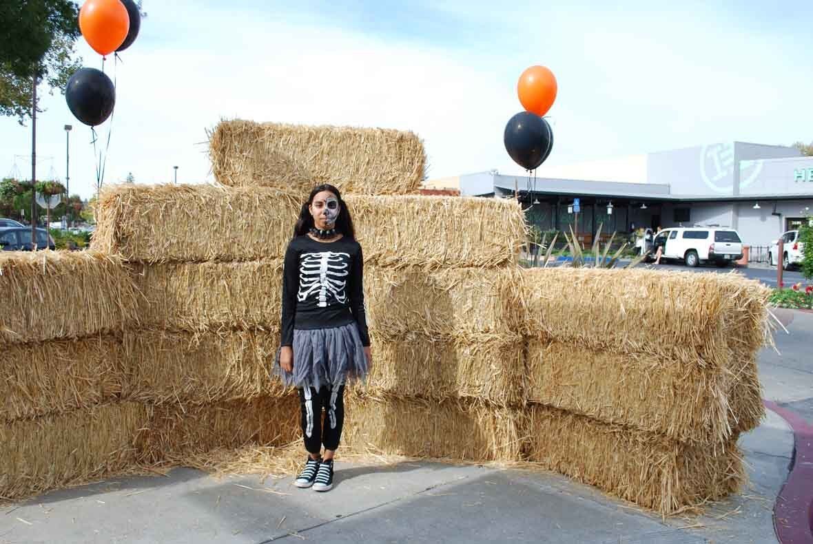 A girl in a skeleton costume is standing in front of a pile of hay bales.
