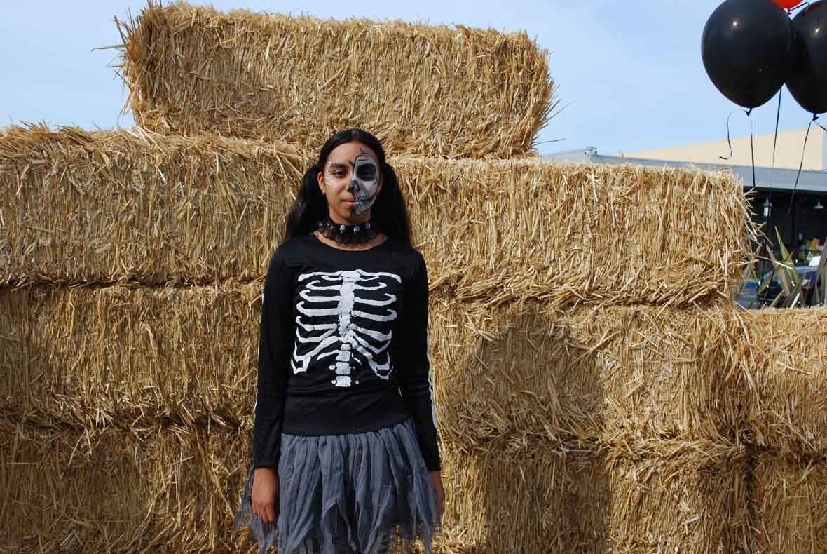 A girl in a skeleton costume is standing in front of hay bales.