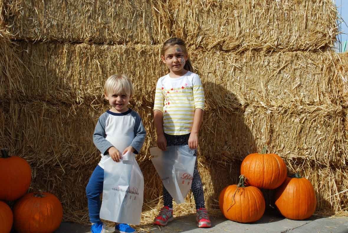 A boy and a girl are standing in front of a pile of hay and pumpkins.