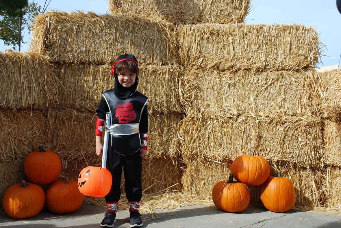 A young boy in a ninja costume is standing in front of hay bales and pumpkins.