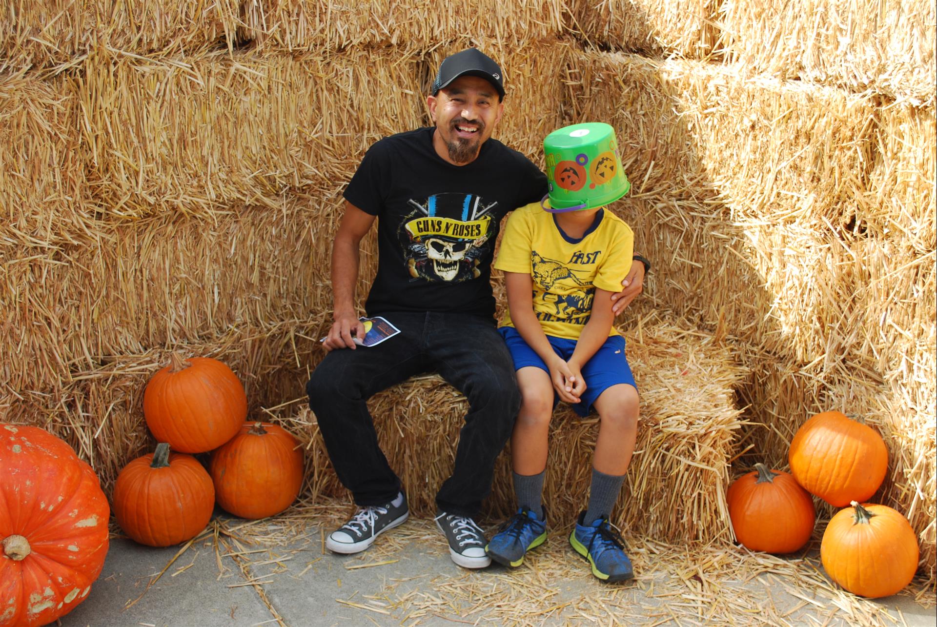 A man and a boy are sitting on hay bales surrounded by pumpkins.