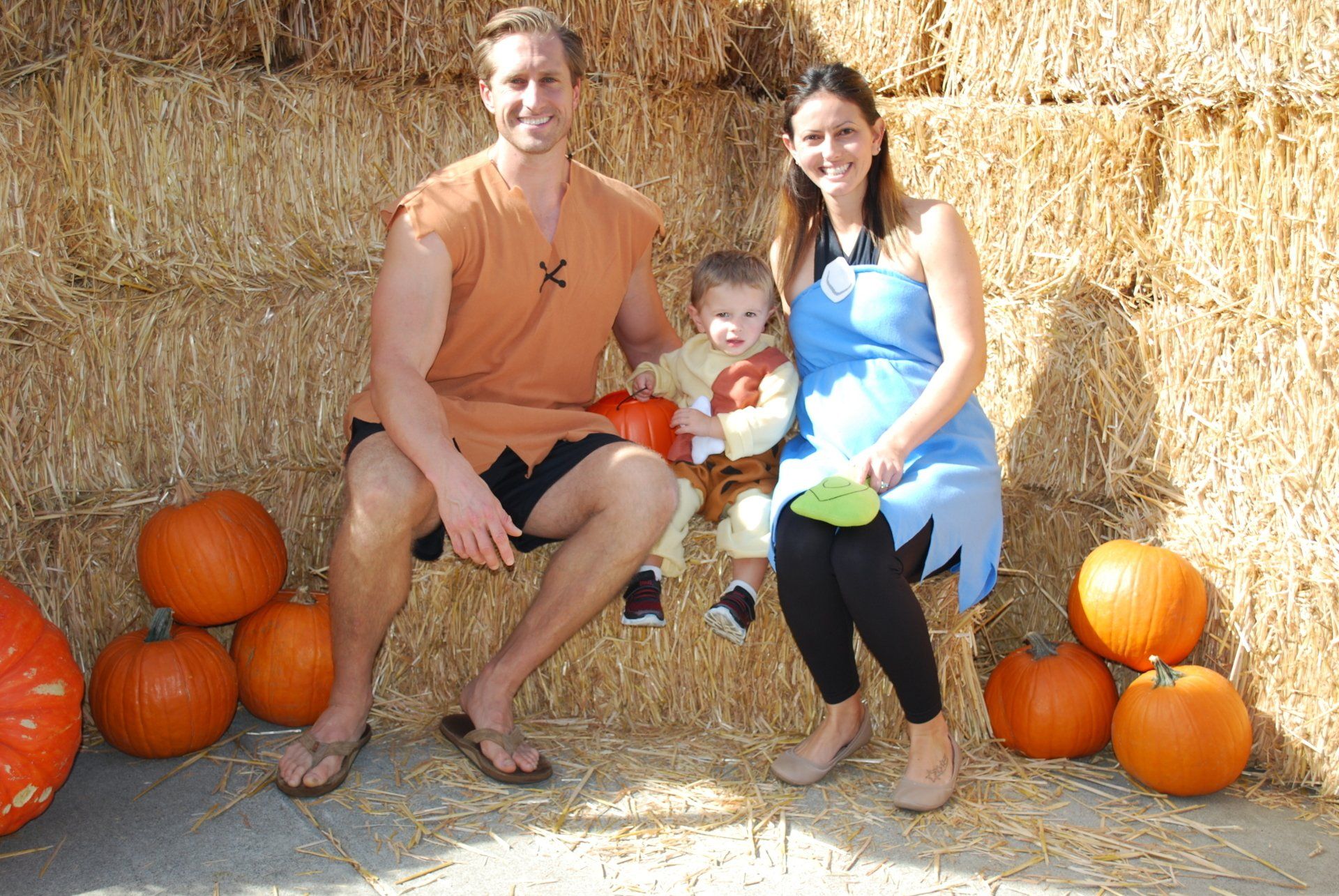 A family is sitting on a bale of hay surrounded by pumpkins
