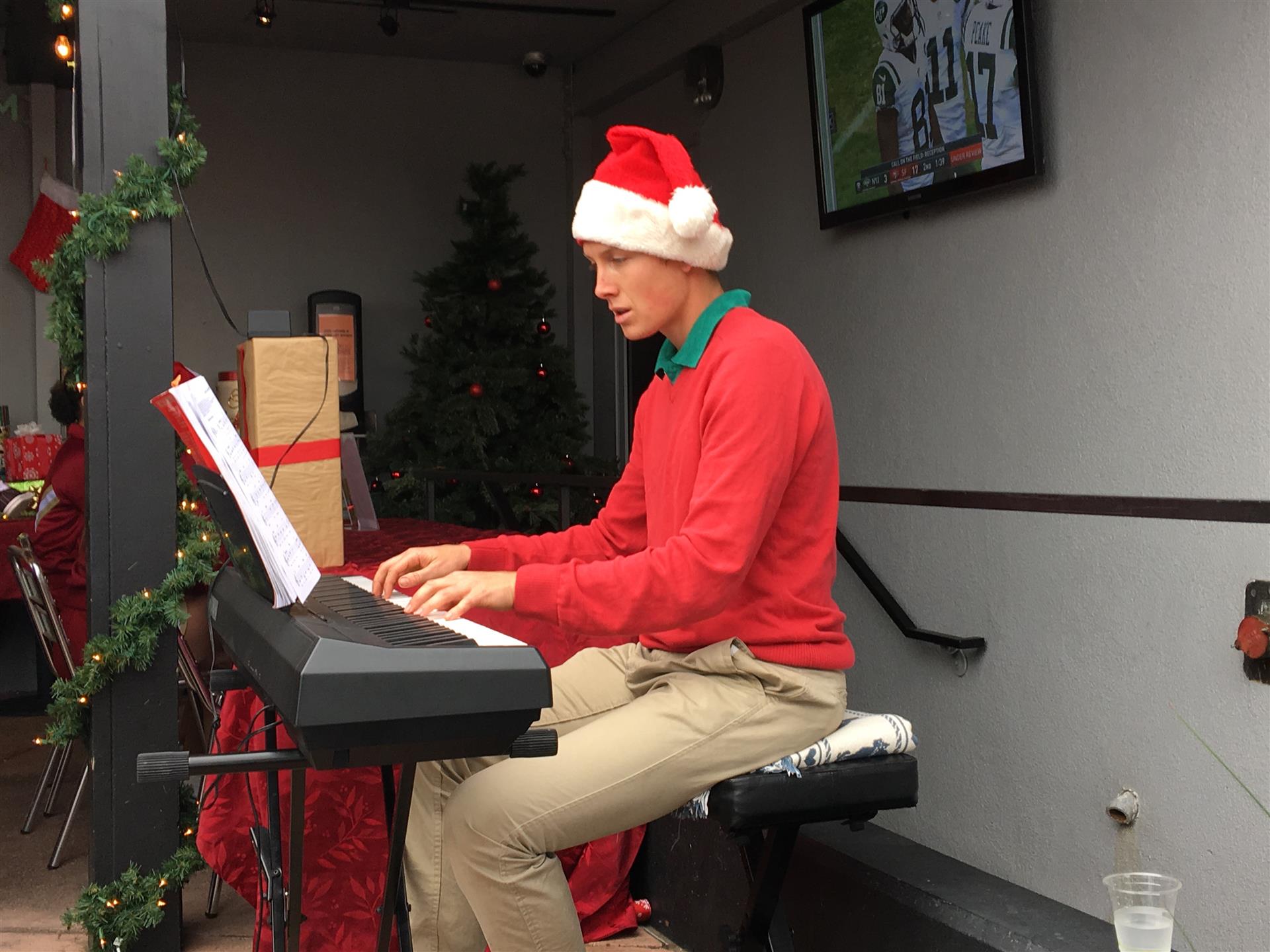 A man wearing a santa hat is playing a piano
