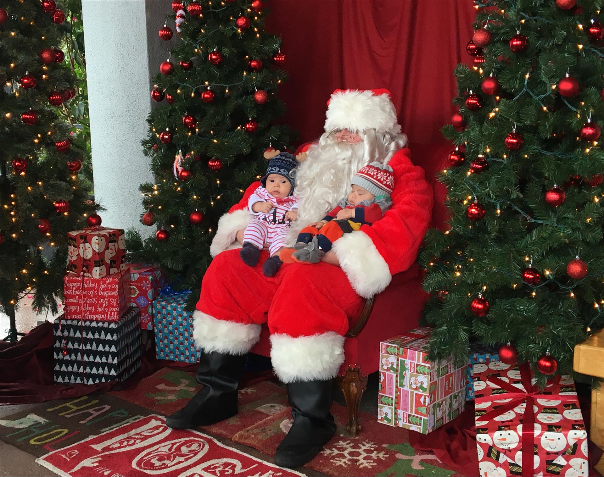 Santa claus is holding a baby in his lap in front of a christmas tree