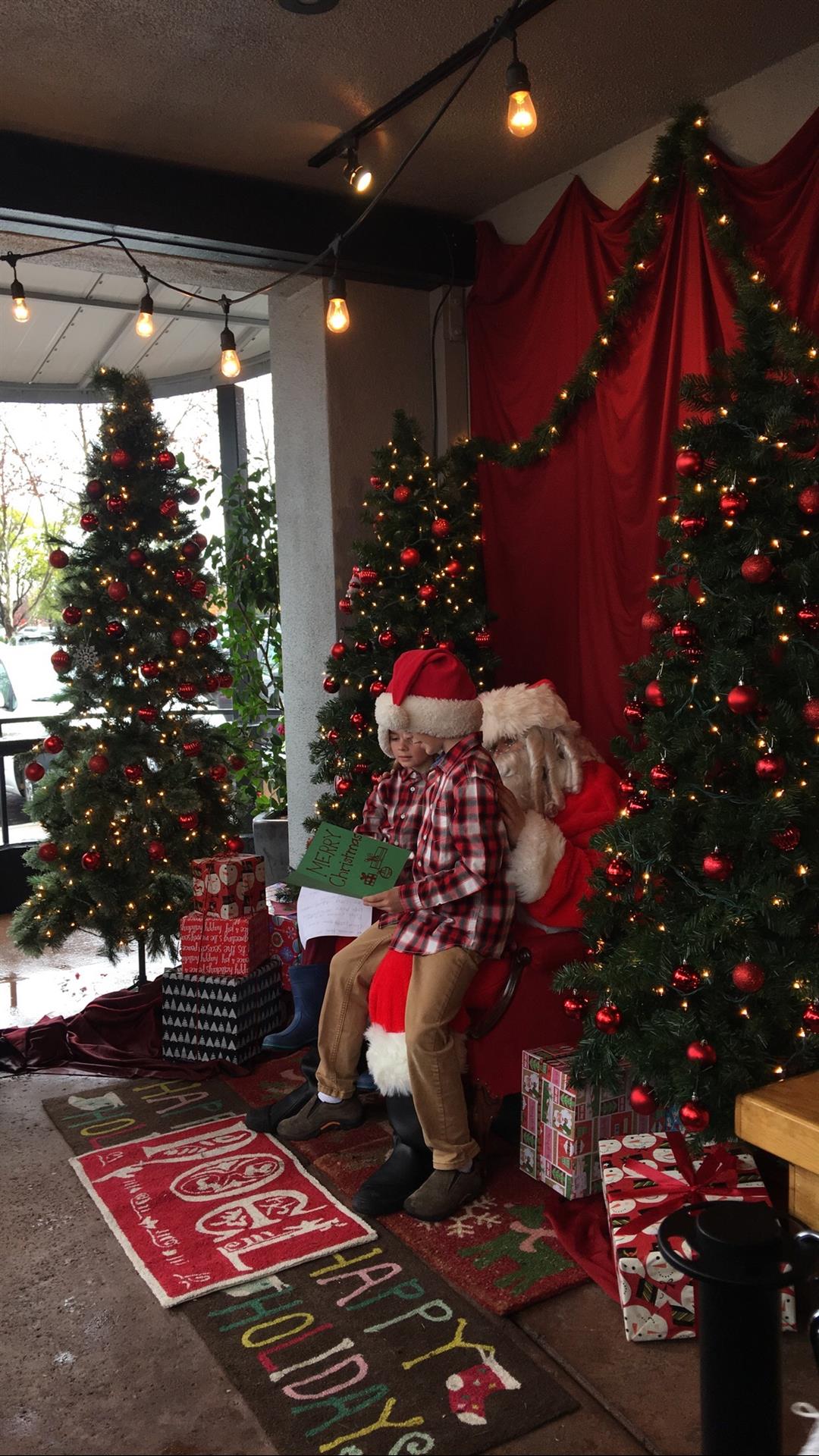 A man is sitting on santa 's lap in front of a christmas tree.