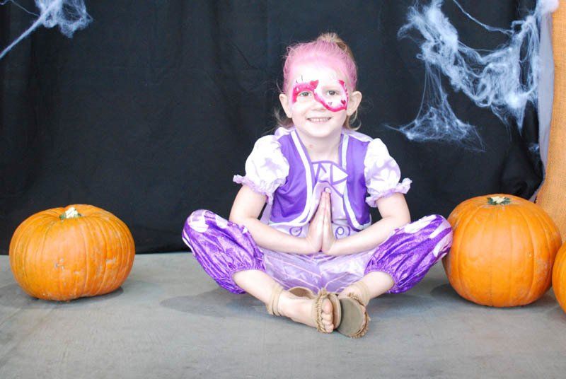 A little girl with pink paint on her face is sitting in front of pumpkins.