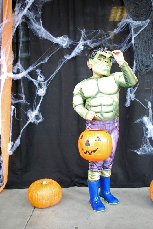 A child dressed as the hulk is holding a pumpkin
