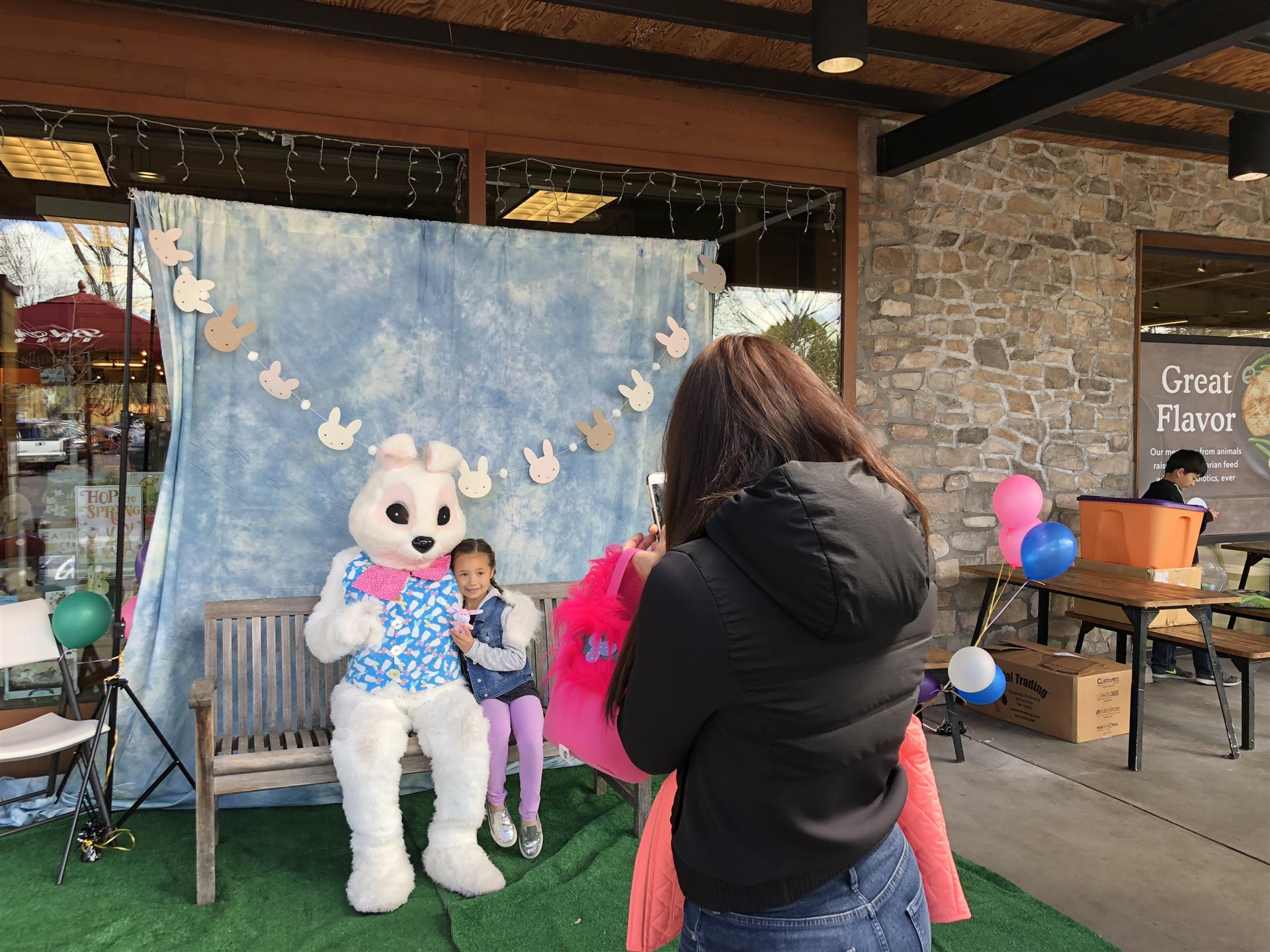 A woman is taking a picture of a little girl and an easter bunny.