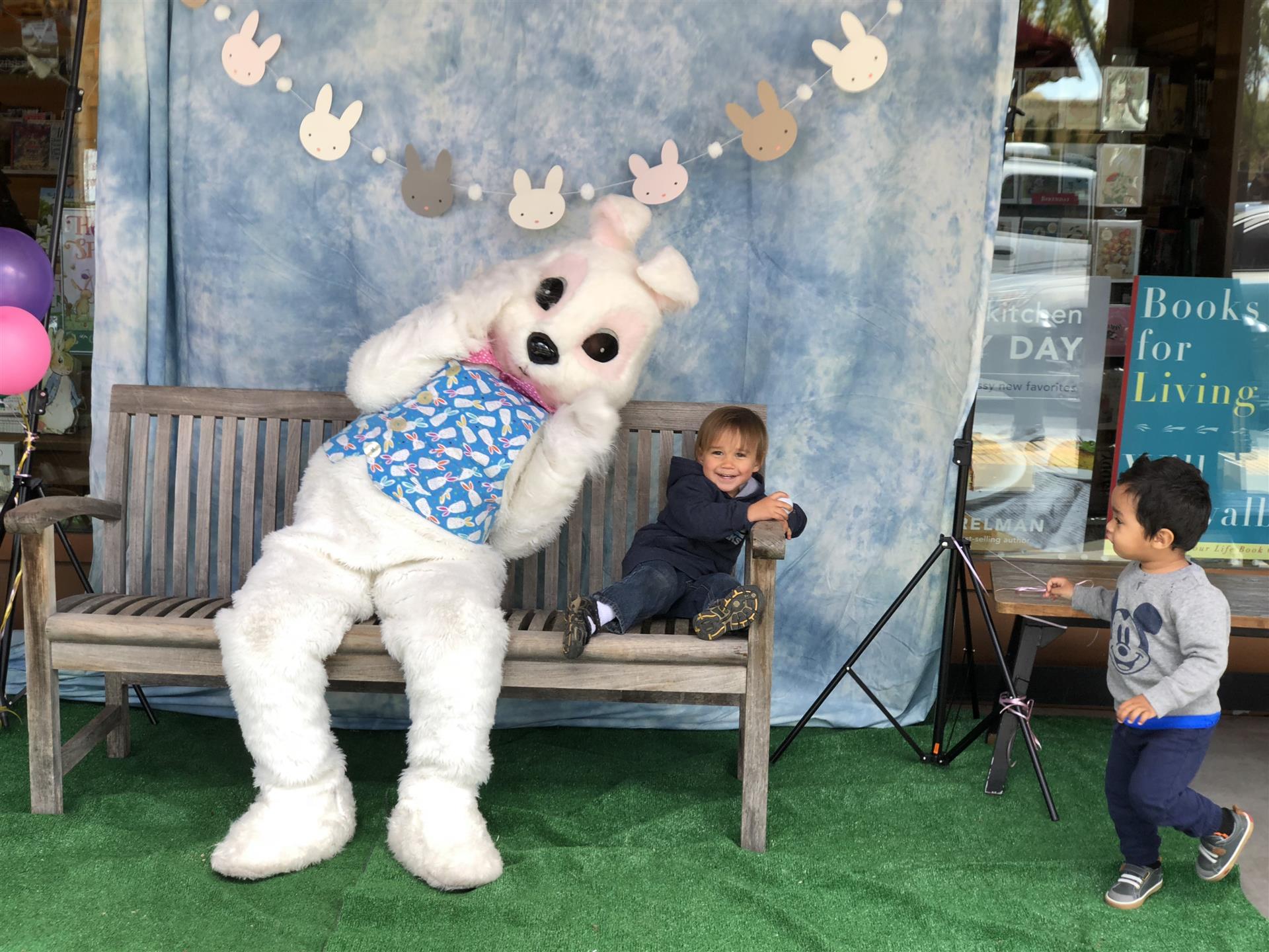 A little boy is sitting on a bench next to a bunny mascot.