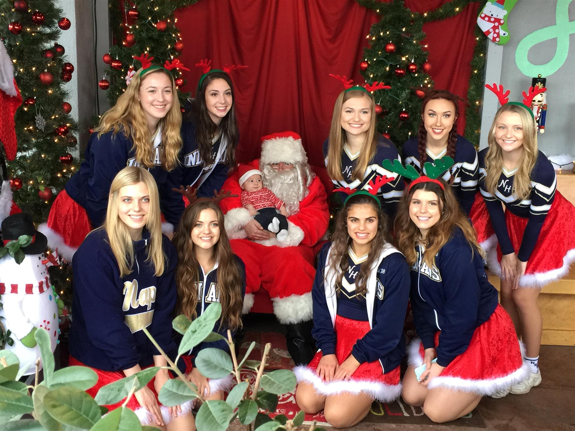 A group of cheerleaders are posing for a picture with santa claus.