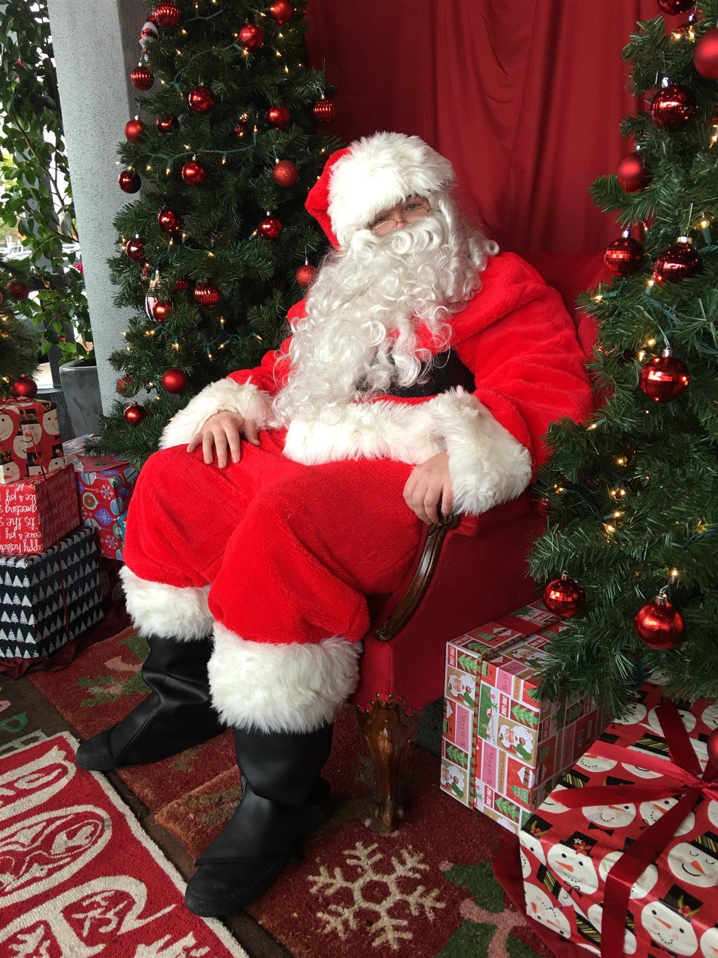 Santa claus is sitting in a chair in front of a christmas tree.