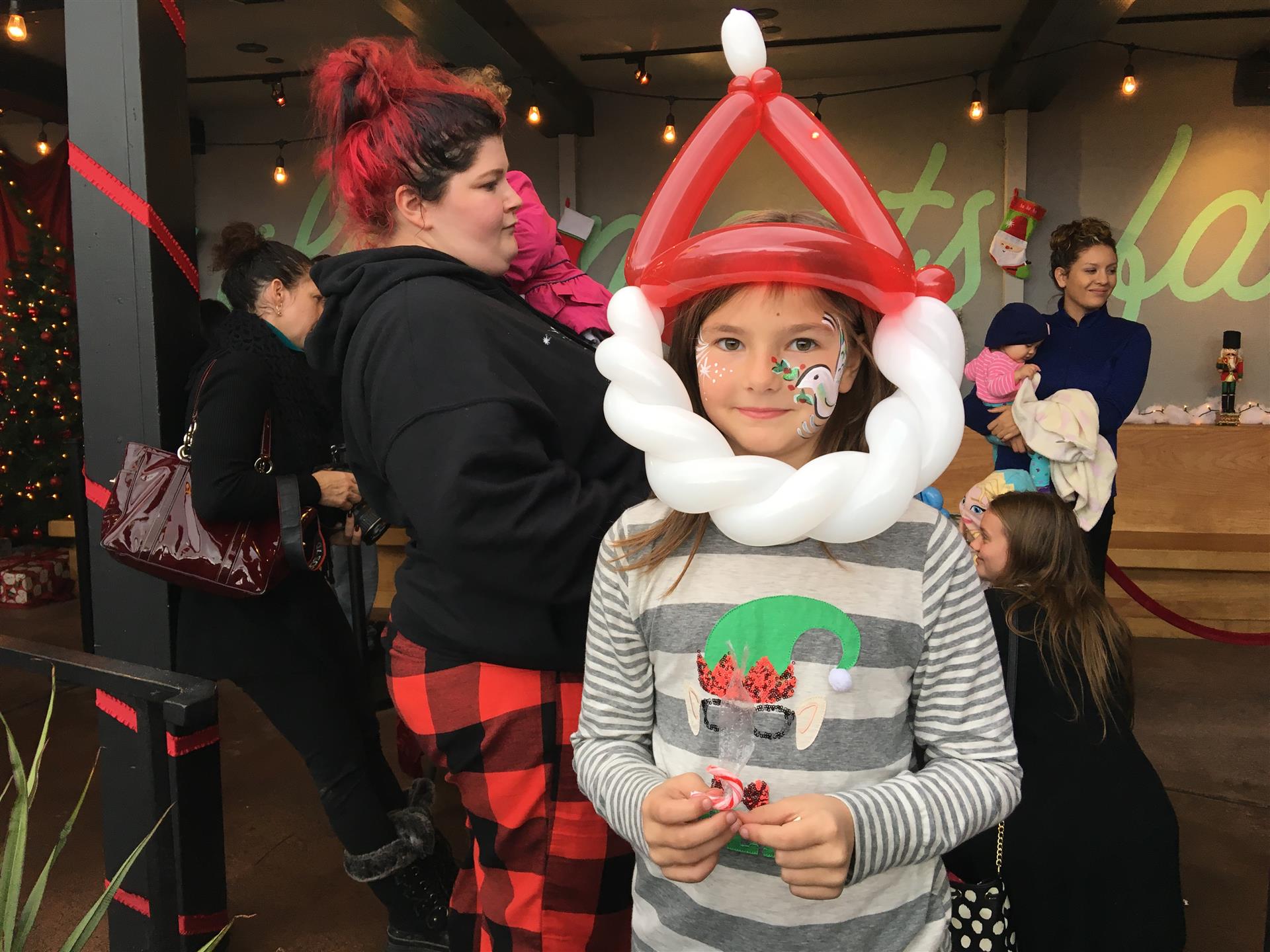A little girl is wearing a santa hat made out of balloons.