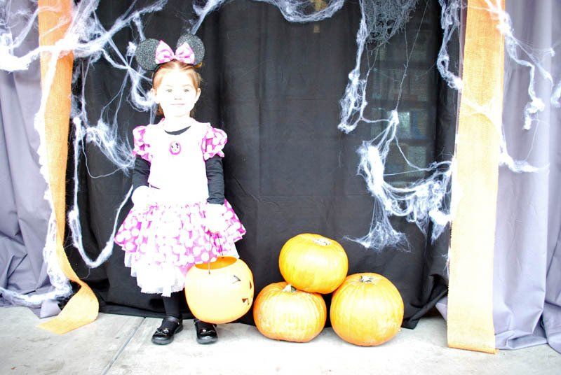 A little girl in a minnie mouse costume is standing next to pumpkins.