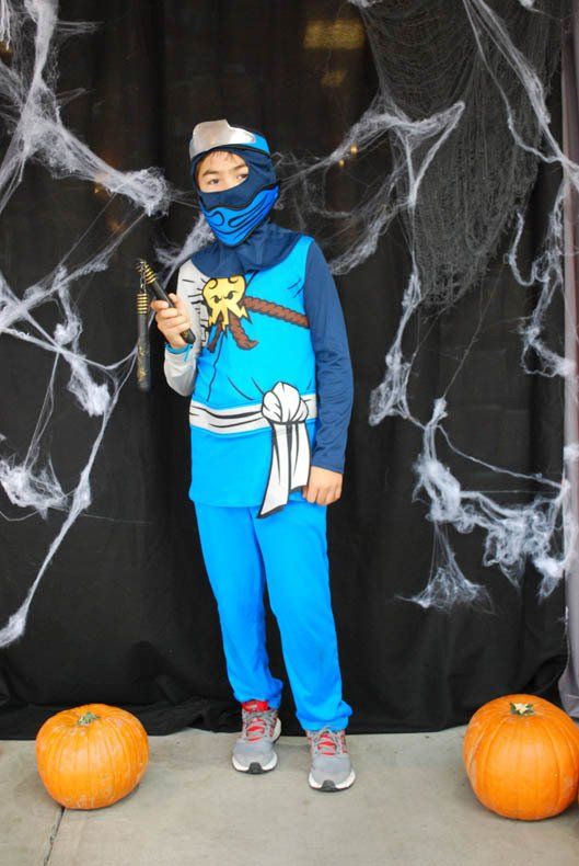 A boy in a ninja costume is standing next to pumpkins