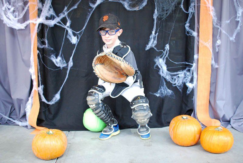 A young boy dressed as a baseball catcher is holding a glove and a ball.