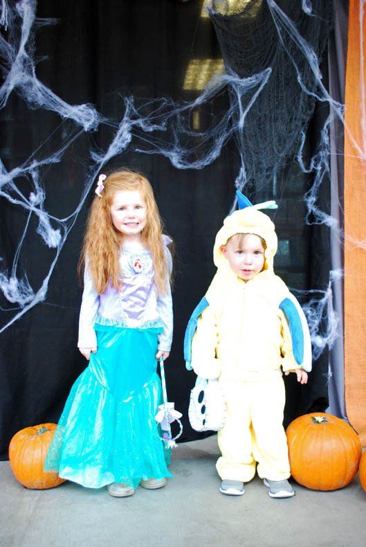 A little girl in a mermaid costume and a little boy in a yellow costume are posing for a picture.