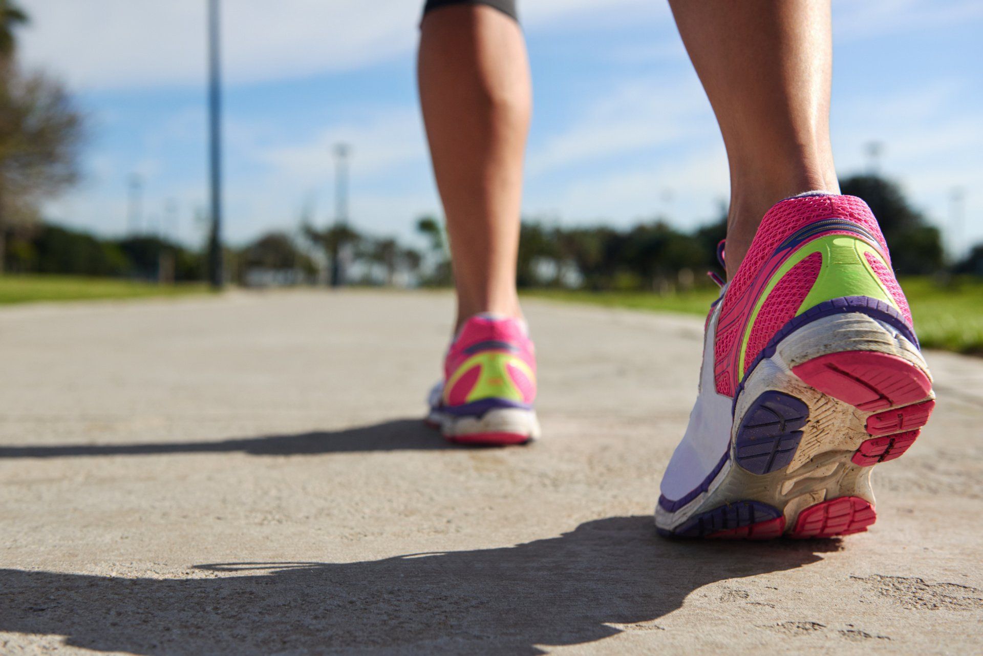 Een persoon loopt op een betonnen pad in roze en witte hardloopschoenen.