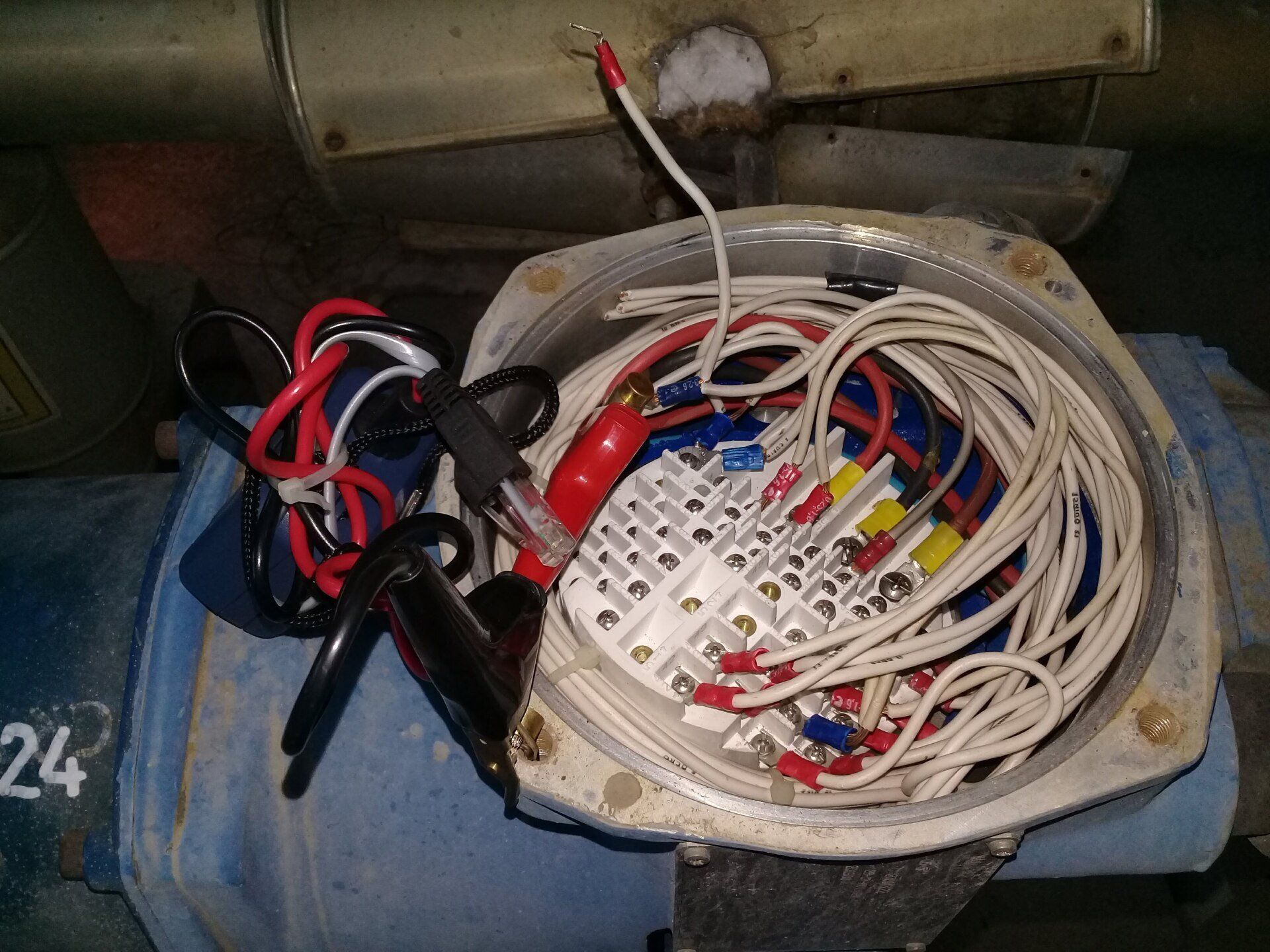 Una caja de conexiones industrial abierta que muestra varios cables conectados a un bloque de terminales blanco en una máquina azul.