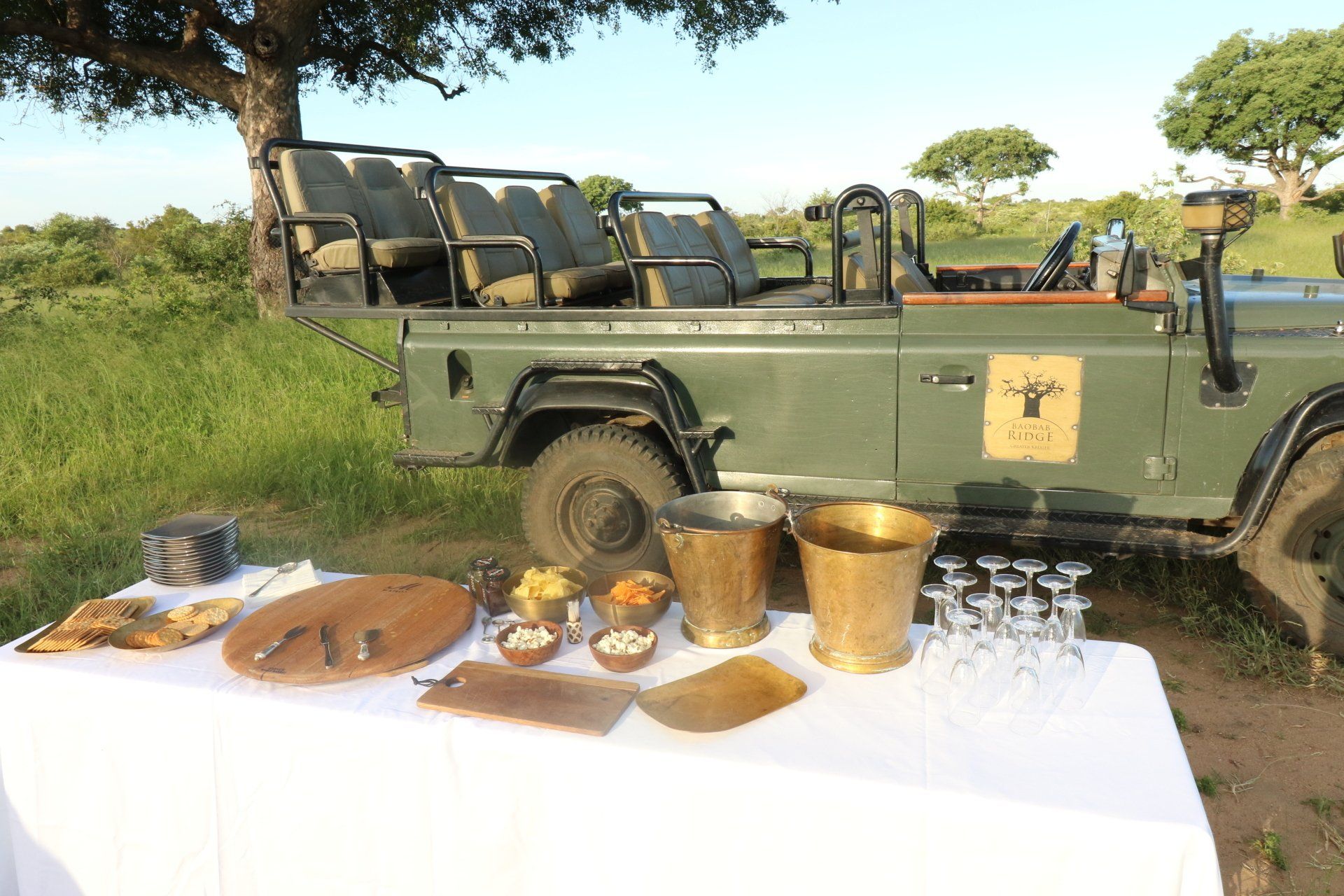 Safari vehicle beside table with brass cups and pottery outdoors