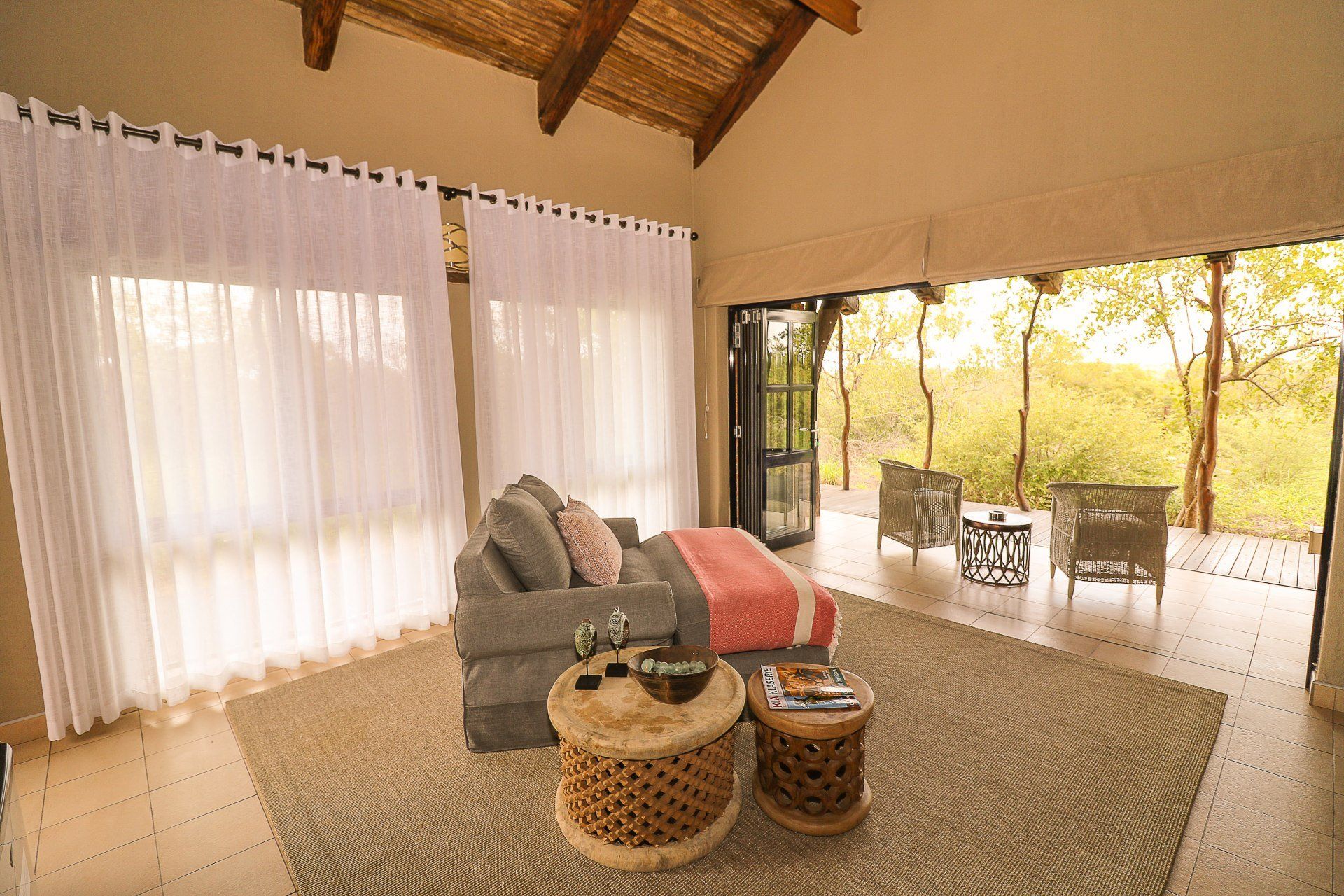 Bright living room with sofa, woven rug, and open patio doors overlooking trees and outdoor seating
