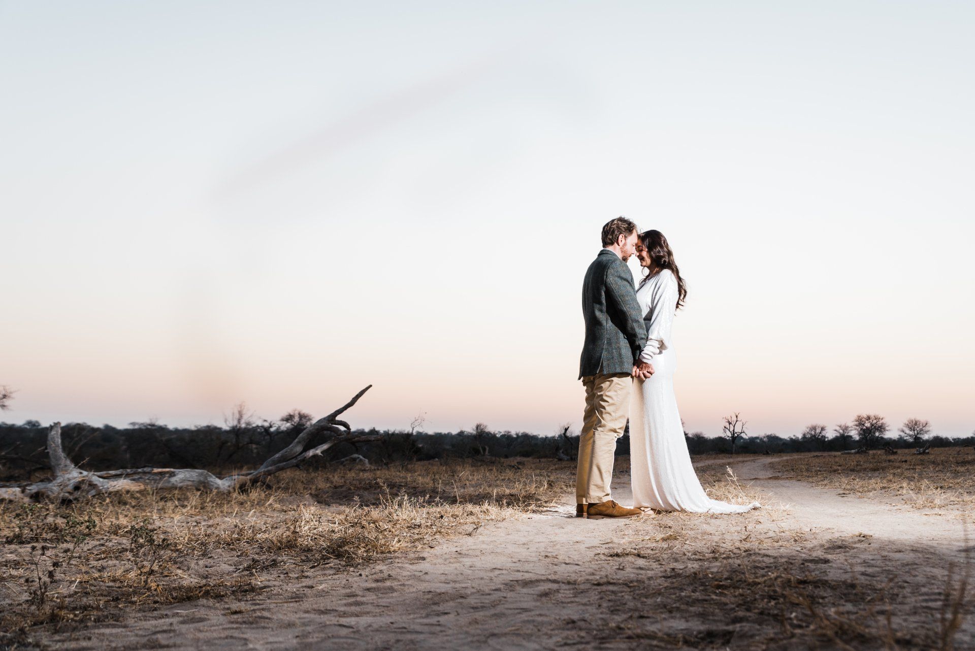 Couple embracing in a barren field at sunset, with a soft pastel sky behind them