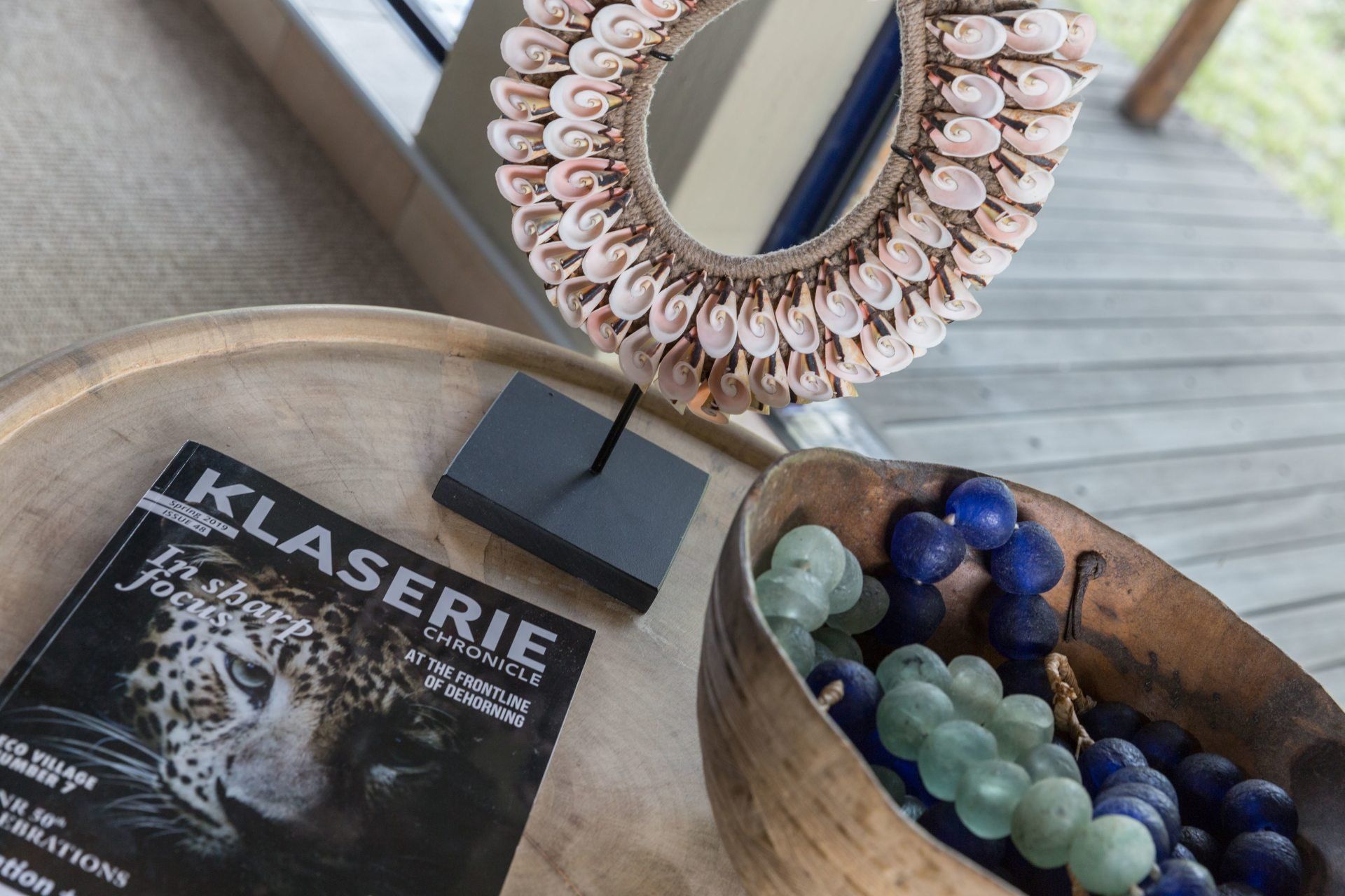 Wooden tray with a black “KLASERIE” package, beaded mirror, and blue-green beaded jewelry pieces.