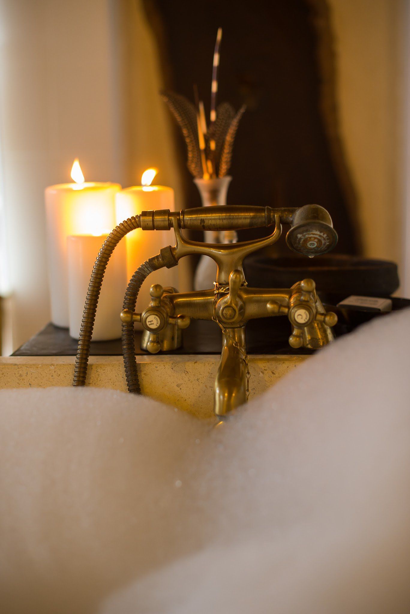Vintage brass faucet with a glowing candle beside it, framed by soft white foreground fabric.