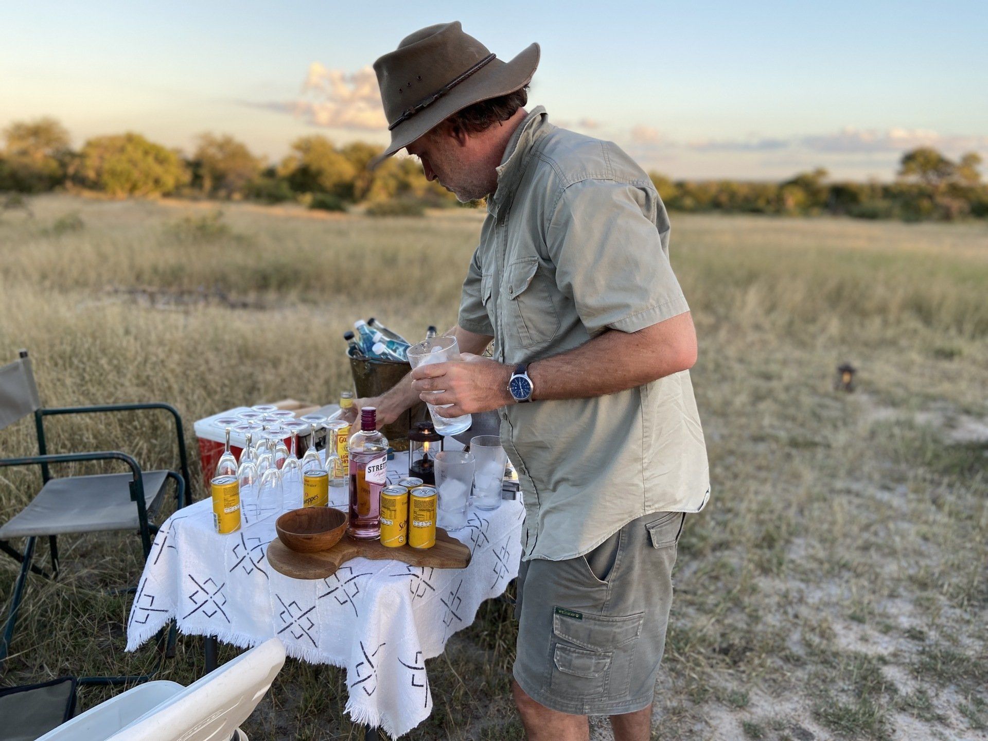 Man arranging items on a picnic table outdoors in a grassy field at sunset
