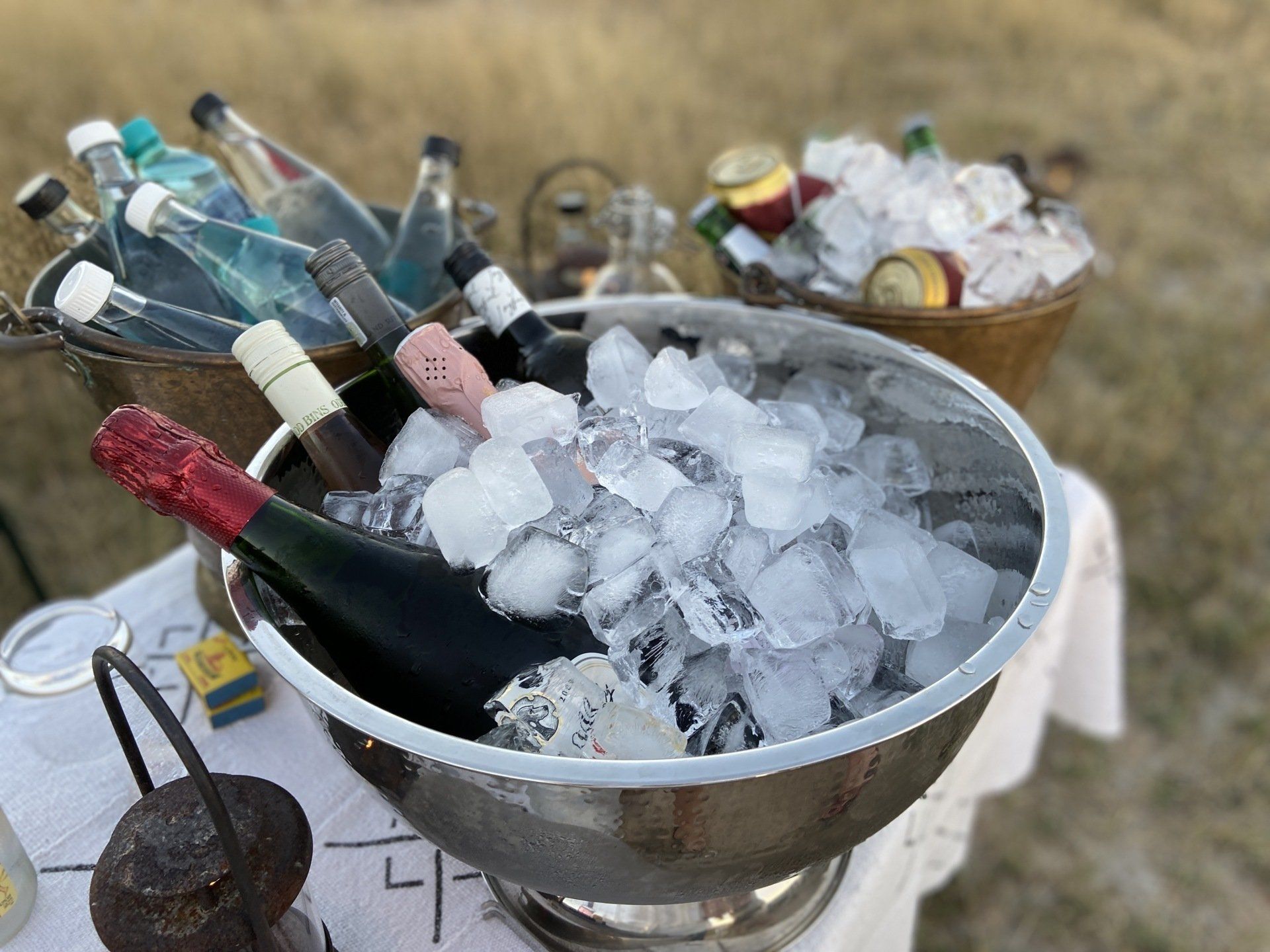 Champagne bottles in ice-filled metal buckets outdoors on dry grass