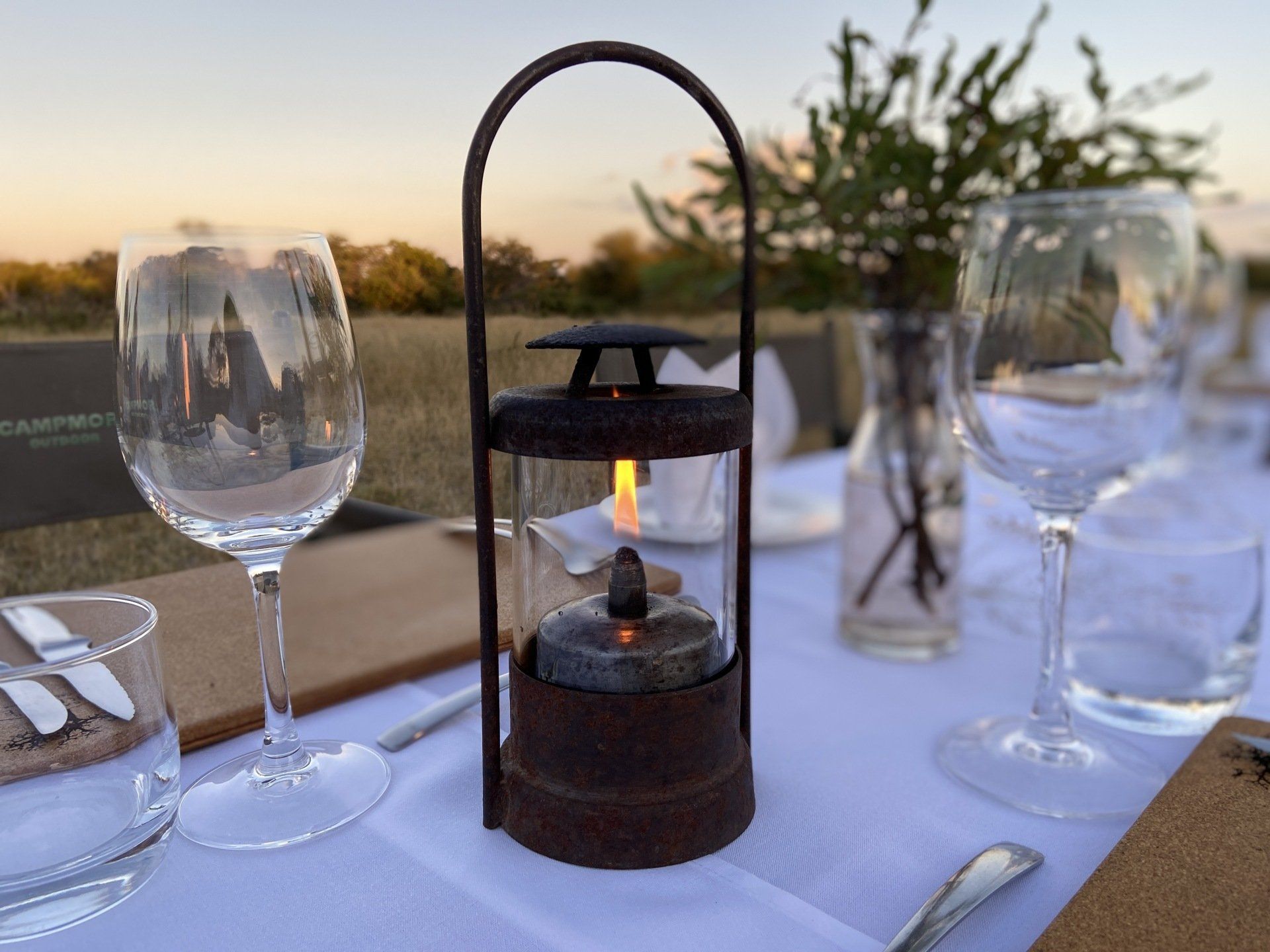 Lantern-lit outdoor dining table set with wine glasses at sunset