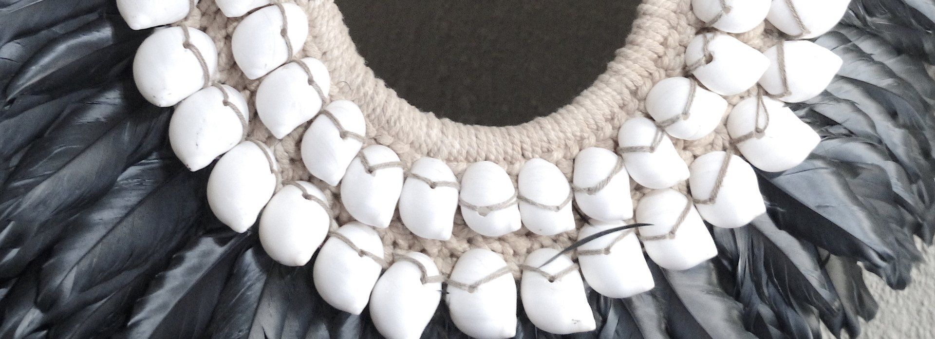 White shell necklace with black feather accents on a woven background