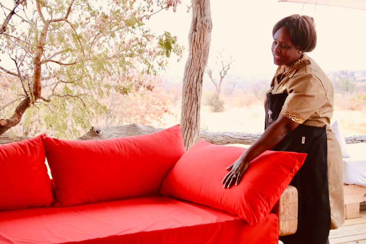 Person adjusting a bright red outdoor couch on a porch beside a tree.