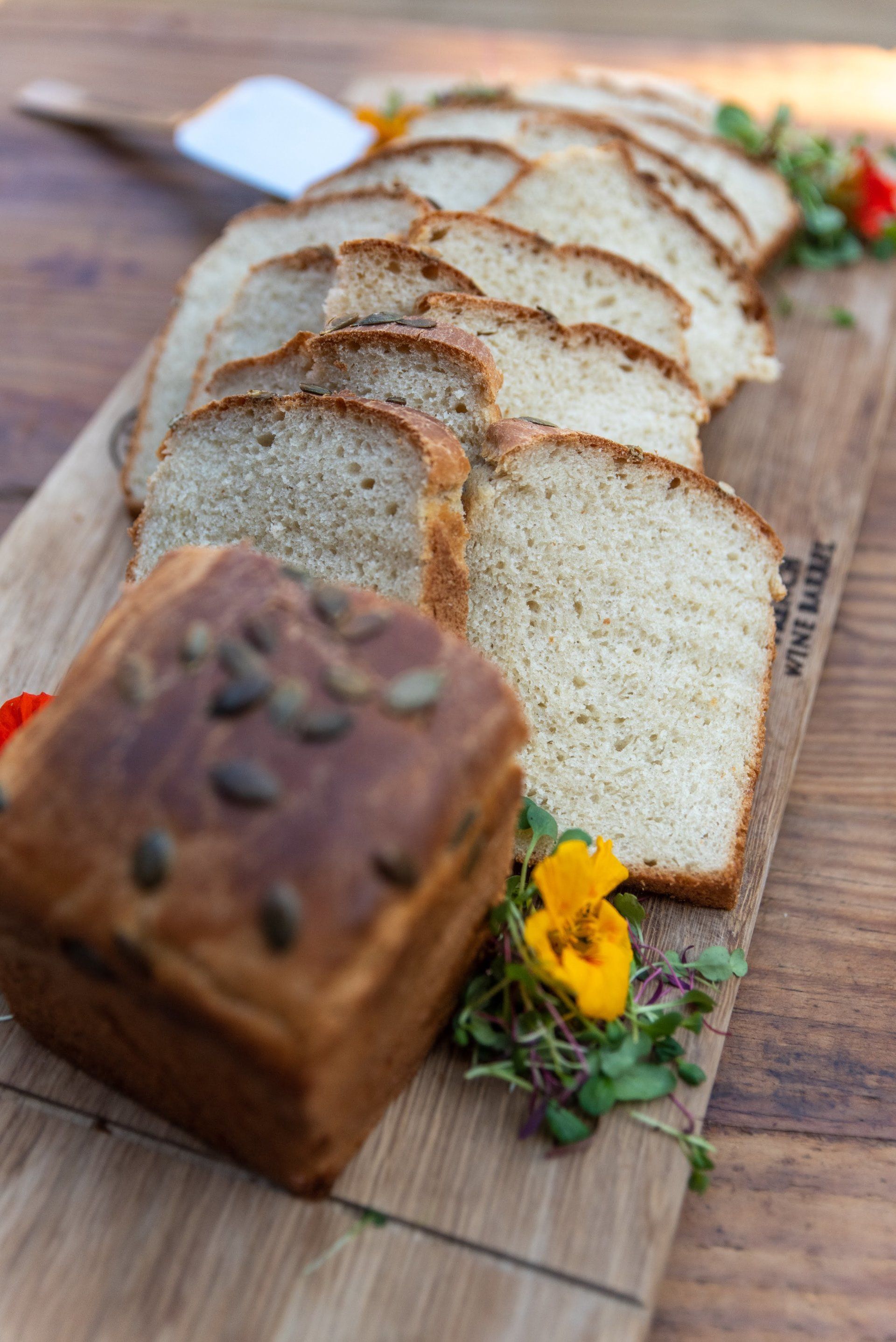 Sliced white bread and a small loaf on a wooden board with flowers and a knife
