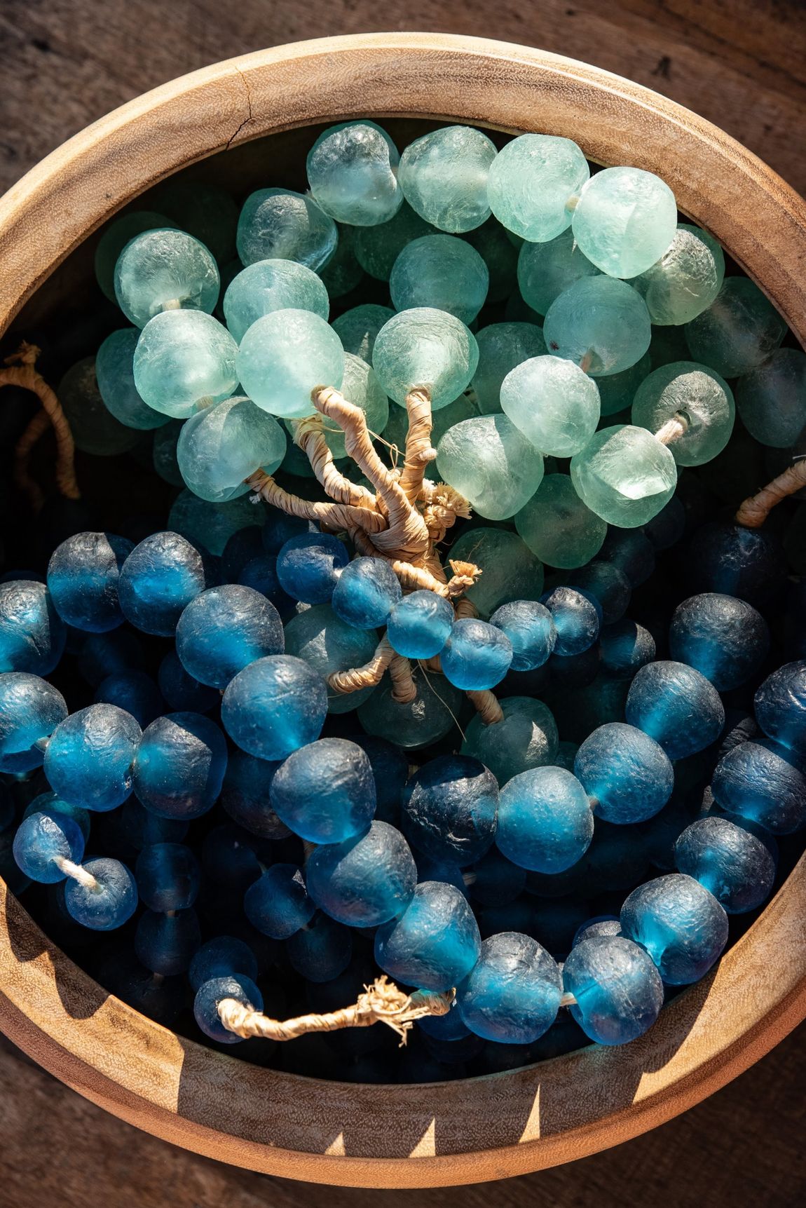 Two strands of blue and mint beads in a round wooden bowl with a small starfish charm