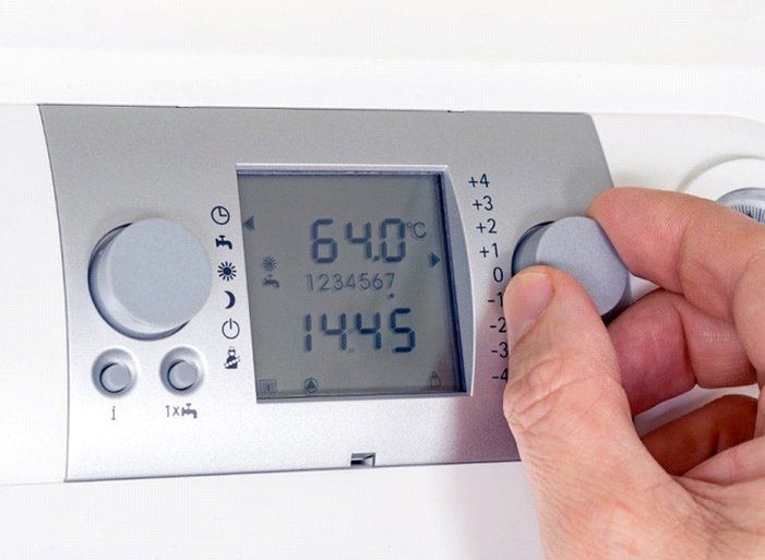 Hand adjusting a thermostat, the display shows 64.0°C and 14:45.