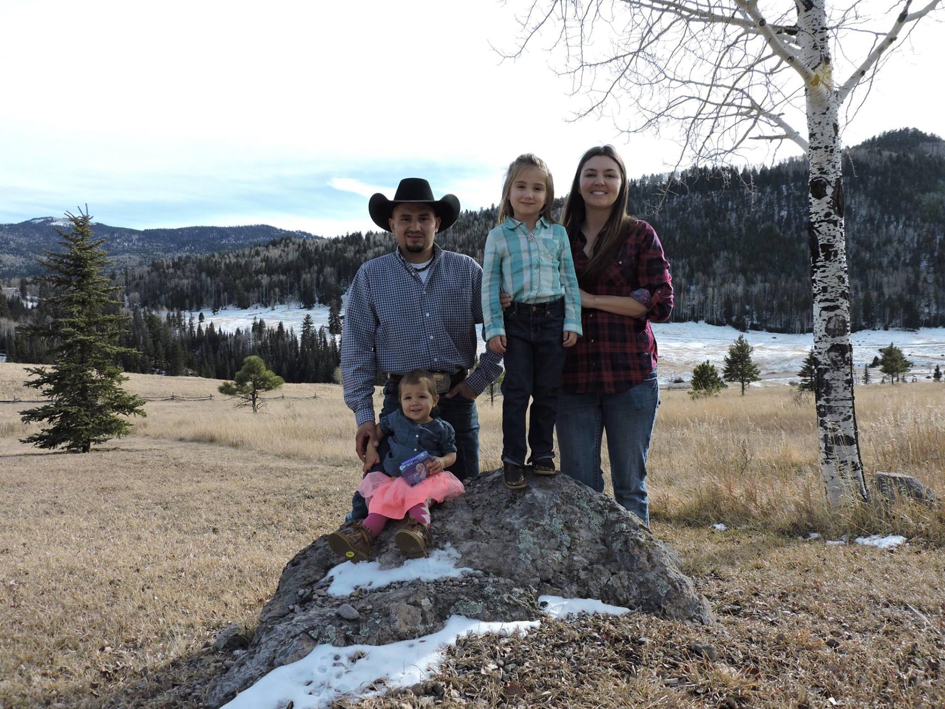 A family is posing for a picture on a rock in a field.