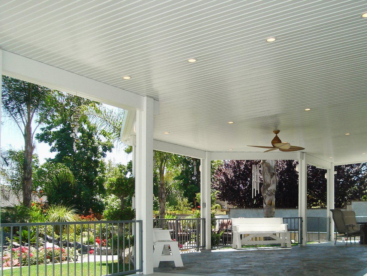 A white porch with a ceiling fan and trees in the background