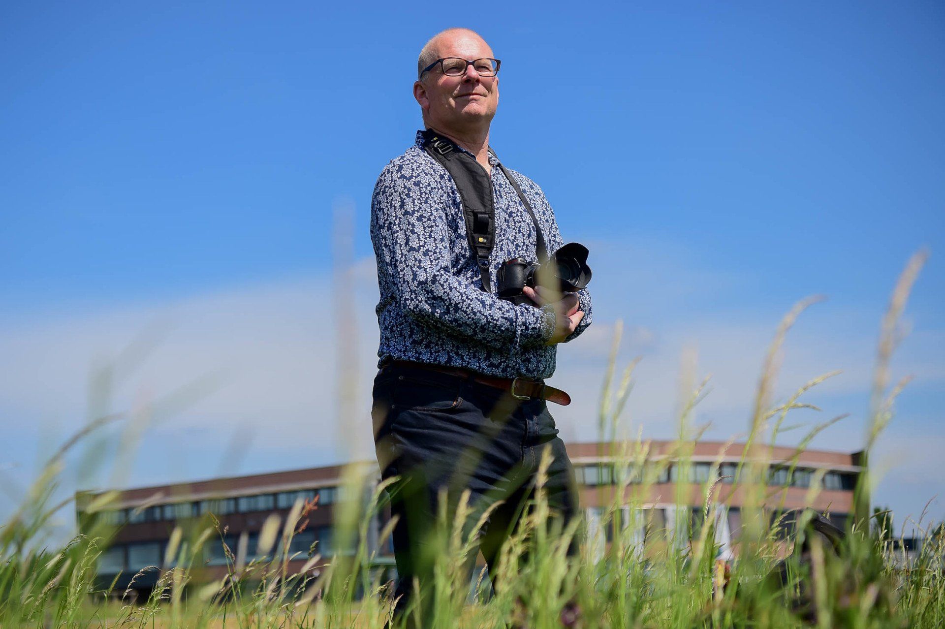 Een man staat in een veld met een camera in zijn handen.