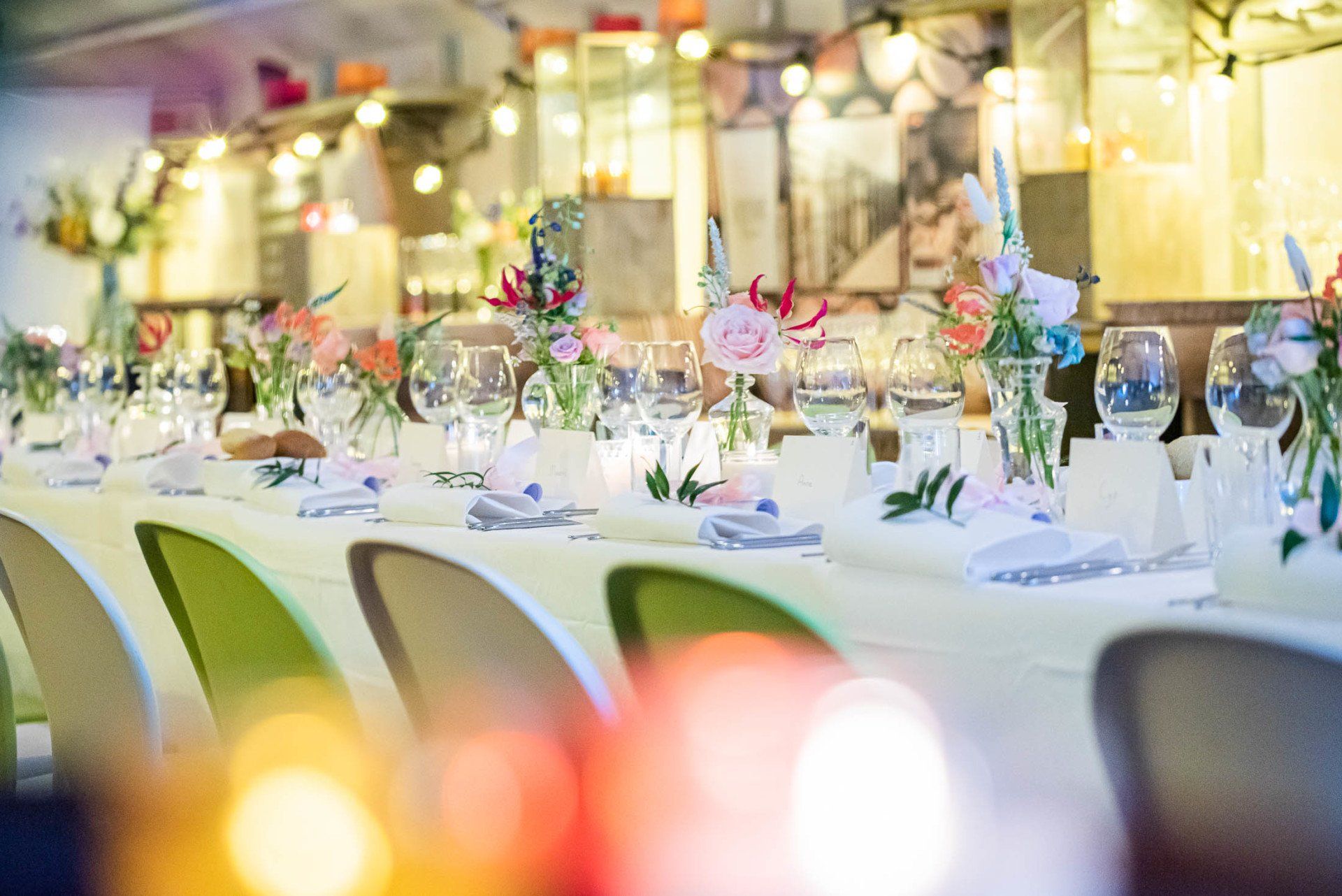 Een lange tafel met veel glazen en bloemen erop.