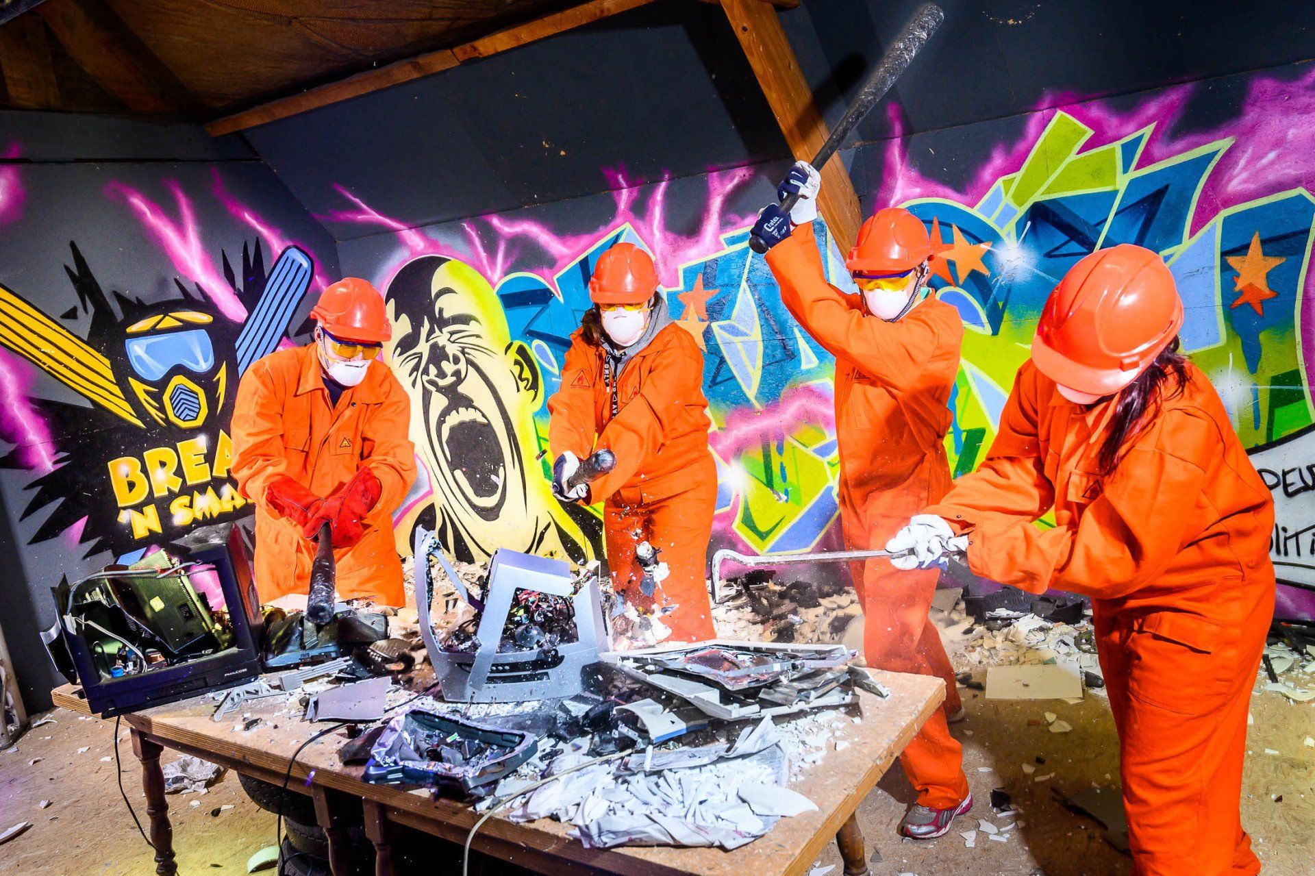 Een groep mensen in oranje overalls en helmen slaat met een hamer een tafel kapot.