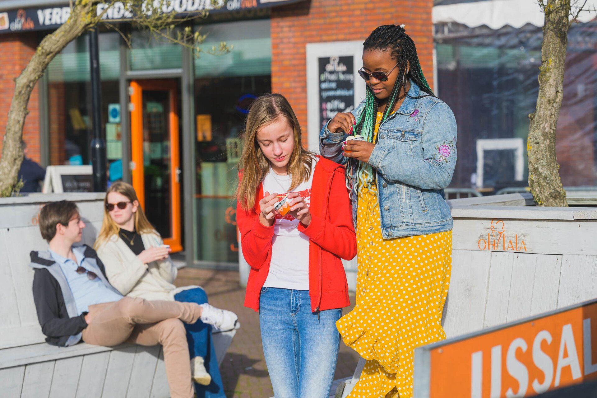 Een groep mensen zit op een bankje en kijkt op hun telefoon.