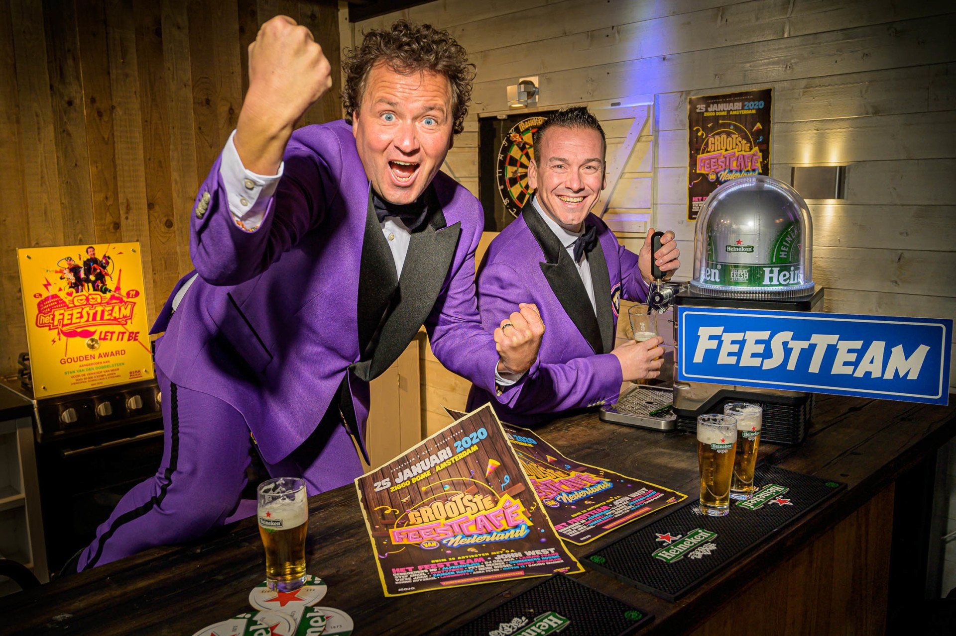 Twee mannen in paarse pakken zitten aan een bar met bierglazen in hun handen.