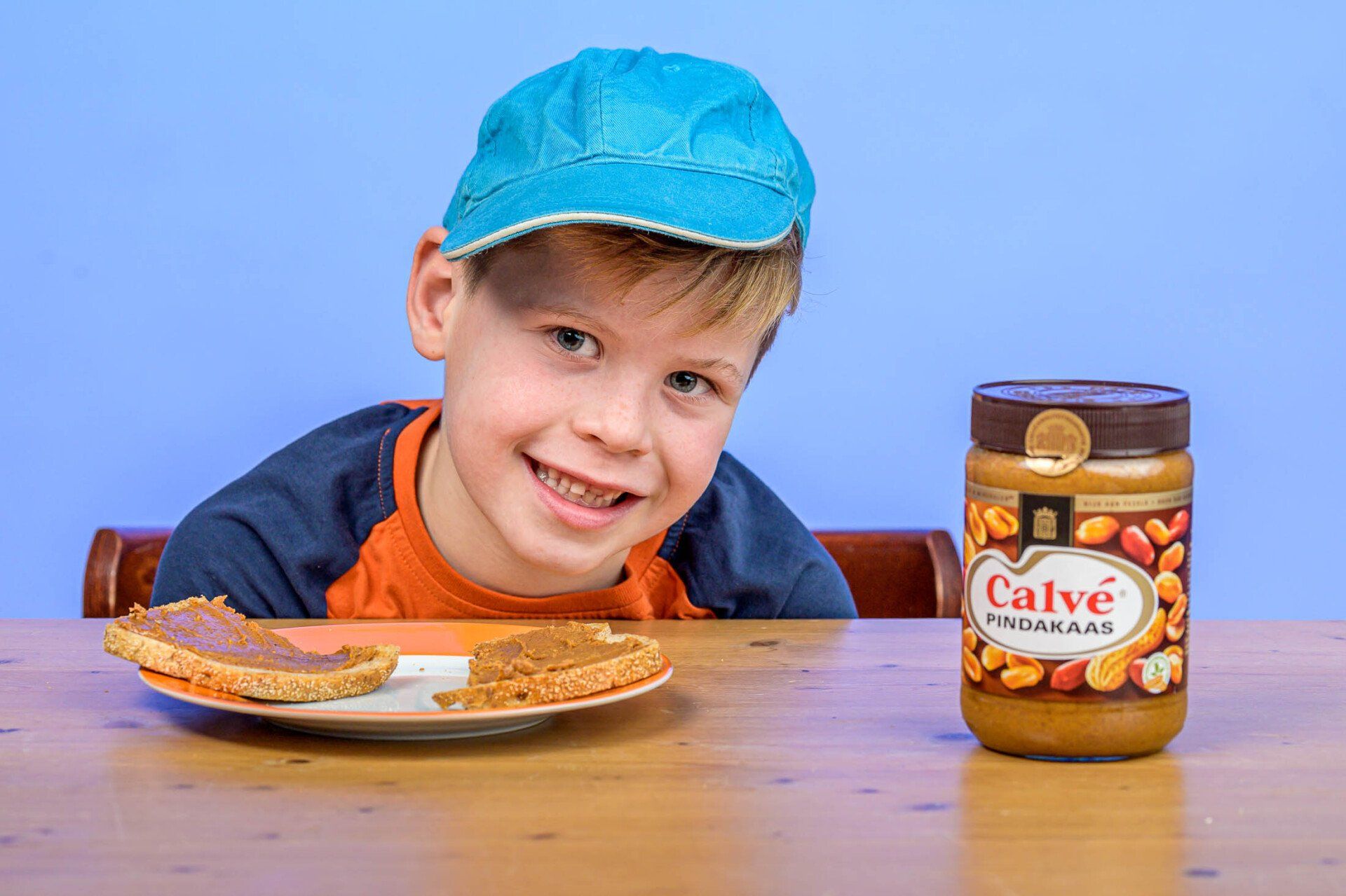 Een jonge jongen zit aan een tafel met een pot Calve pindakaas.