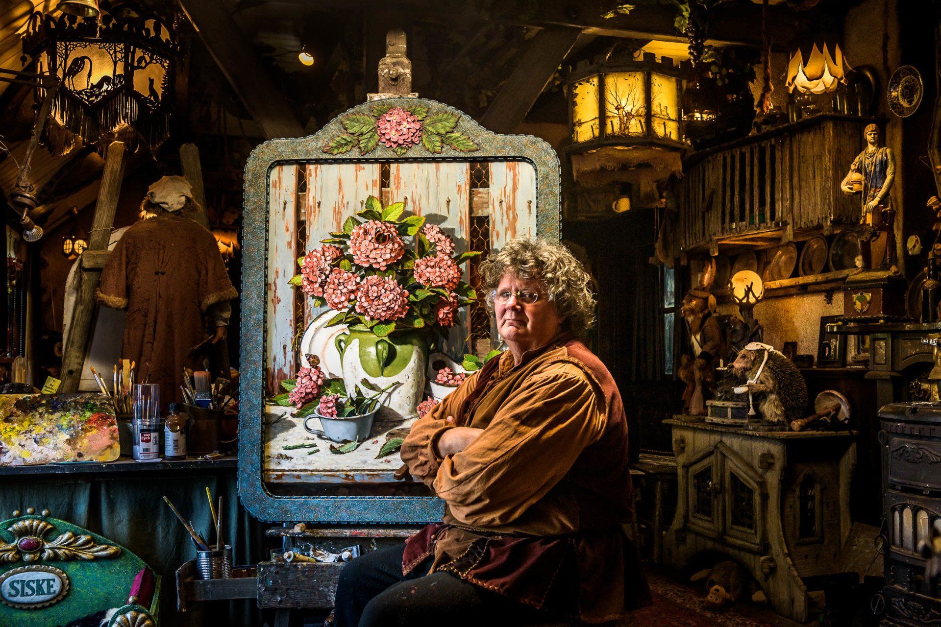 Een man zit voor een groot schilderij van bloemen.