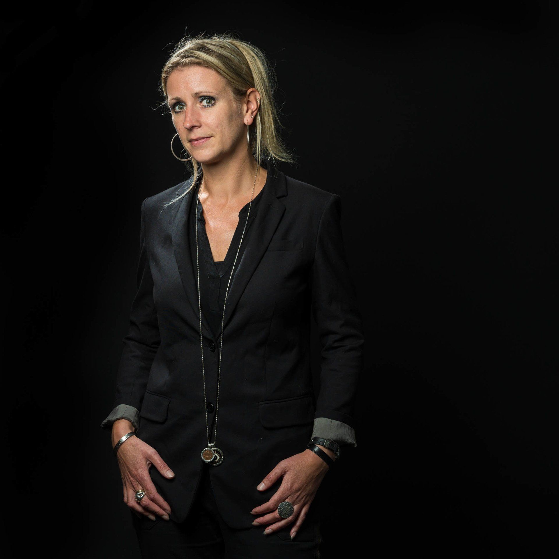 Een vrouw in een zwart pak staat voor een zwarte achtergrond