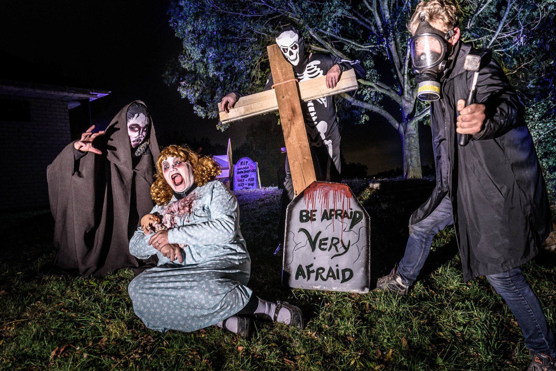 Een groep mensen verkleed in Halloween-kostuums poseert voor een foto voor een graf.