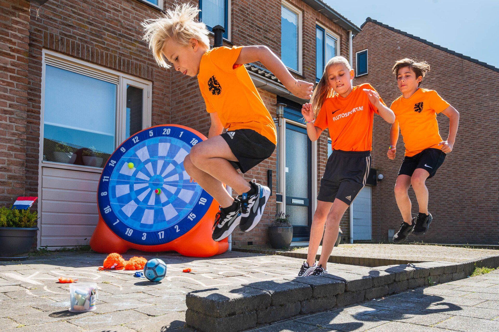 Drie kinderen springen in de lucht voor een dartbord.