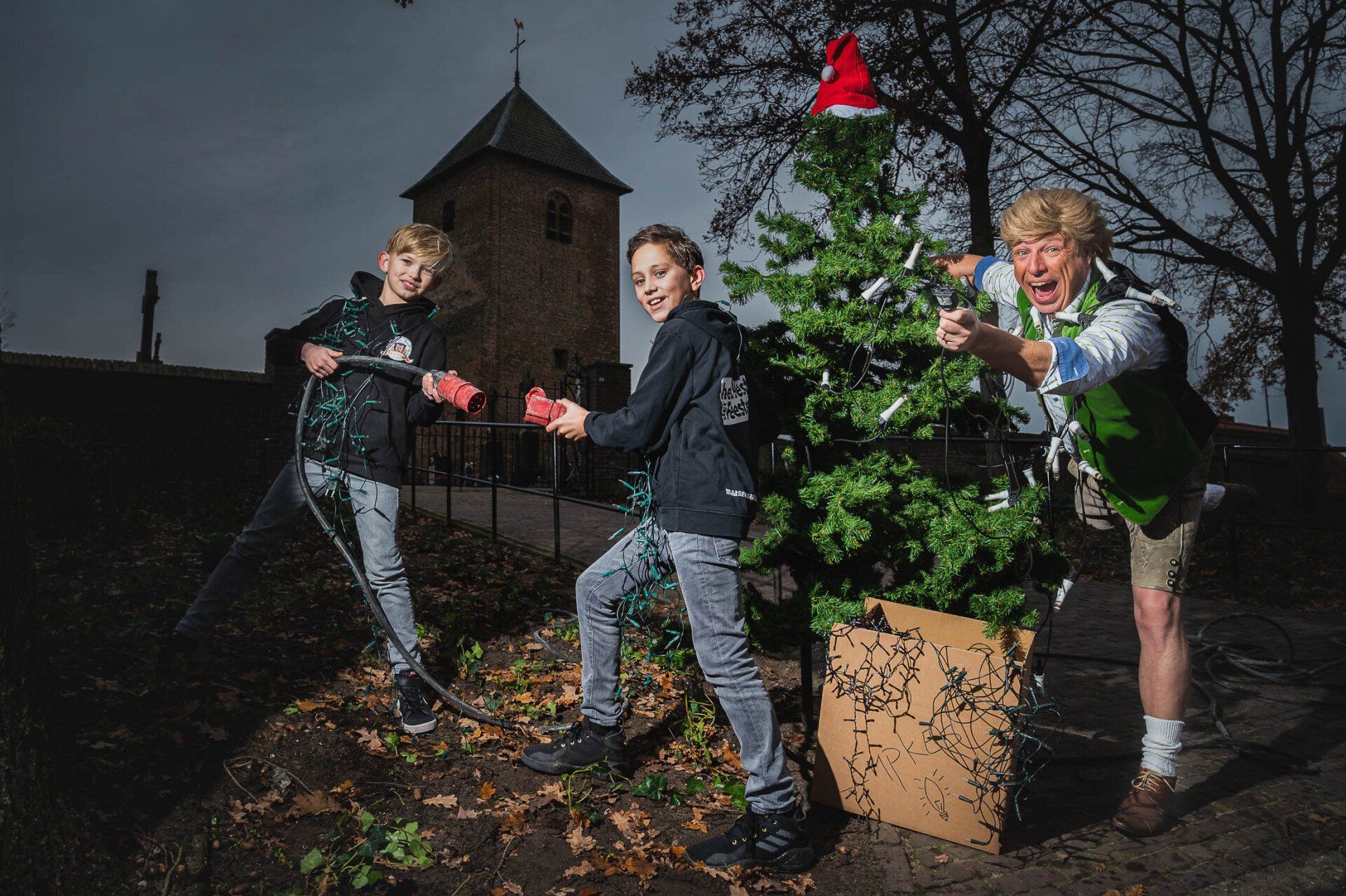 Drie jonge jongens zijn buiten een kerstboom aan het versieren.